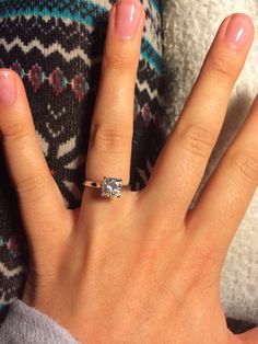 a woman's hand with a diamond ring on her left hand and a sweater in the background