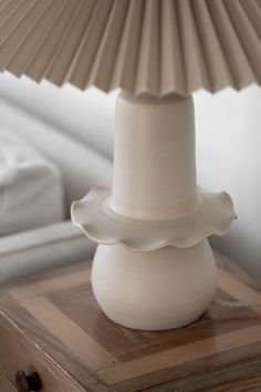 a white vase sitting on top of a wooden table next to a large lamp shade