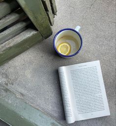 a cup of tea next to an open book and a lemon slice on the ground