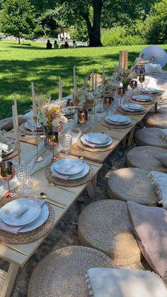 a long table set with place settings and plates on it in the middle of a park