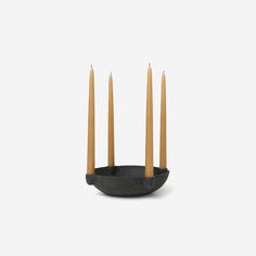 four candles are in a black bowl on a white background