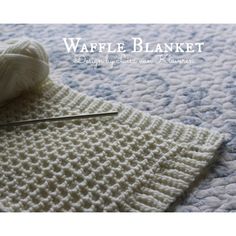 a white knitted blanket sitting on top of a bed next to a ball of yarn