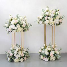 two tall vases with flowers and greenery on them