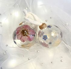 two glass ornaments with flowers on them sitting on a white cloth covered tablecloth next to pearls and tulle