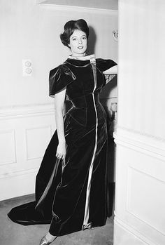 an old black and white photo of a woman in a long dress standing next to a wall