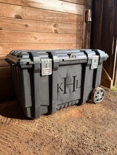 two black coolers sitting on the ground next to a wooden fence and building with wood siding