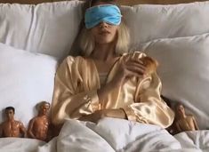 a woman laying in bed with blindfold on her face and several toy figures behind her