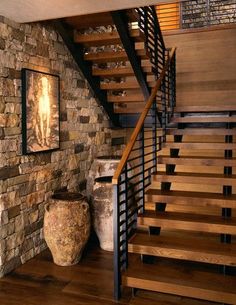 there is a stone wall and stairs in this room with wood floors, two vases on either side of the staircase