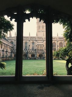 an open window looking out onto a large building with trees in the foreground and grass on the other side