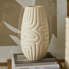 a white vase sitting on top of a table next to a stack of books and a plant