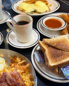 a table topped with plates of breakfast foods and cups of coffee next to each other