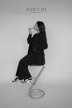 a woman sitting on top of a metal chair eating something out of her mouth while wearing black and white sneakers