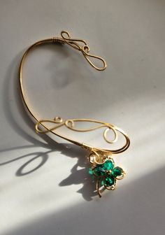 A wirewrapped gold-tone right earwrap with an emerald bicone crystal shamrock drop Gold Metal Wire Wrapped Ear Cuff, Elegant Gold Wire-wrapped Ear Cuff, Elegant Gold Wire Wrapped Ear Cuff, Gold Wire Wrapped Ear Cuff As Gift, Gold Hand-wrapped Dangle Jewelry, Green Handmade Ear Cuff For Gift, Gold Hand Wrapped Dangle Jewelry, Wire Wrapped Dangle Jewelry For May Birthstone, Gold Hand-wrapped Wrap Earrings As Gift