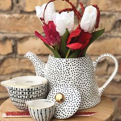 a polka dot tea pot with flowers in it and two cups on the table next to it