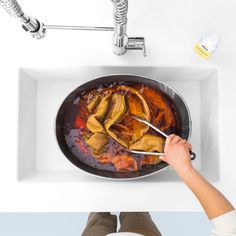 a person stirring food in a pan on a white counter top with the lid down