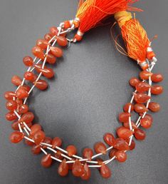 an orange necklace with beads and tassels on a black surface, next to a red tassel