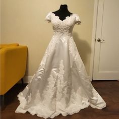 a white wedding dress on display in front of a yellow chair and door with a black mannequin standing next to it