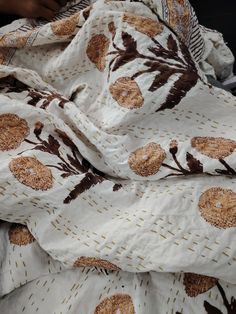 a blanket with brown flowers on it is laying on top of a chair and someone's hand reaching for something in the background