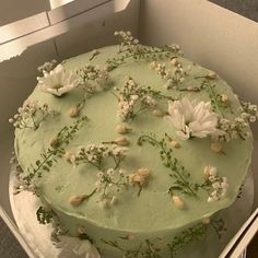 a green cake with white flowers on top in a box