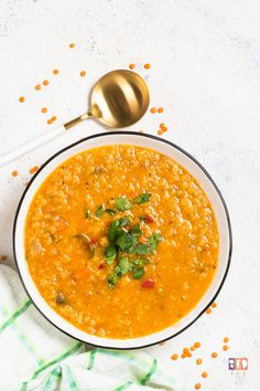 a white bowl filled with red lentula soup and garnished with cilantro