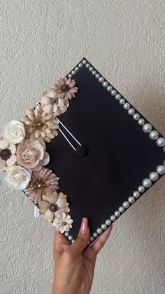 a hand holding a black graduation cap with flowers on the side and pearls around it