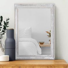 a large silver framed mirror sitting on top of a wooden shelf next to a vase