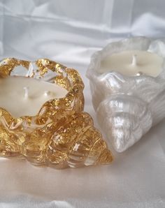 two candles sitting next to each other on a white cloth covered tablecloth with a gold - plated candle holder in the middle