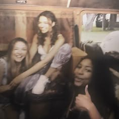 three young women are sitting on the back of a bus and posing for a photo