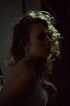 a woman with curly hair sitting in front of a mirror looking off to the side