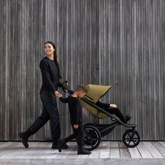 a woman walking next to a child in a stroller and another person holding the baby's hand