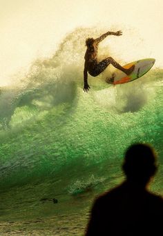 a man riding a surfboard on top of a wave in the ocean at sunset