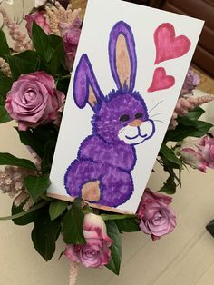 a painting of a purple bunny with hearts on it's face and flowers in the background