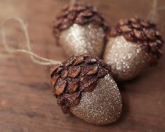 three christmas ornaments on a wooden table with twine and glittered pinecones