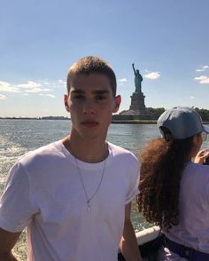 two people on a boat in front of the statue of liberty, looking at the camera