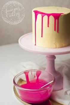 a cake with pink icing sitting on top of a table next to a bowl