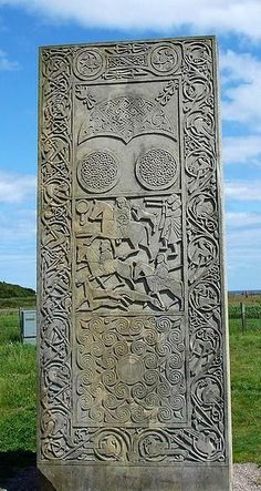 a large stone sculpture sitting in the middle of a grass covered field with a sky background