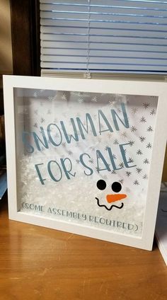 a snowman for sale sign is displayed in a white frame on a wooden table