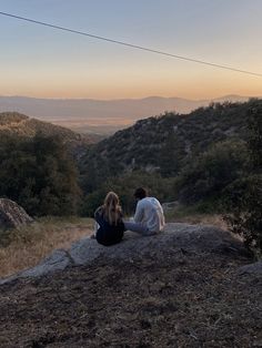 two people sitting on top of a rock looking out at the hills and valleys in the distance