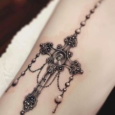 a cross tattoo on the side of a woman's leg with beads and pearls