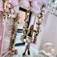 a woman standing in front of a pink and white floral arch with flowers on it