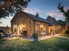 an old brick building with lights on in the front yard at sunset or dusk, surrounded by greenery and patio furniture