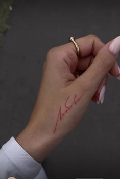 a woman's hand with a small tattoo on her left wrist and the word love written in red ink