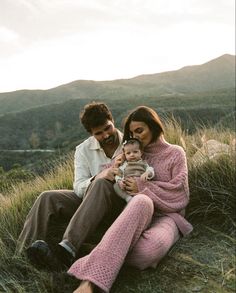 a man and woman are sitting in the grass with a baby