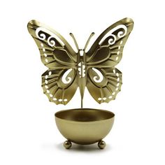 a gold butterfly figurine sitting on top of a bowl with a white background