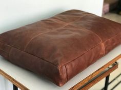 a brown leather cushion sitting on top of a wooden table next to a white wall