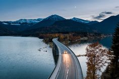 a car is driving on the road over water with mountains in the background at night