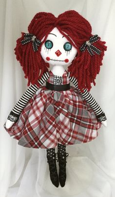 a doll with red hair and blue eyes wearing a plaid dress is posed on a white background