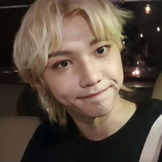 a young man with blonde hair and black shirt smiling at the camera while sitting in a car