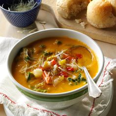 a white bowl filled with soup next to rolls on top of a wooden cutting board