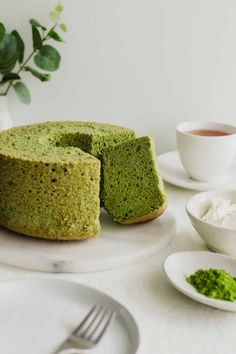 a green cake sitting on top of a white plate next to a cup and saucer